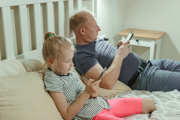 Man and girl child relaxing on bed using separate smartphones. Digital addiction in family life....