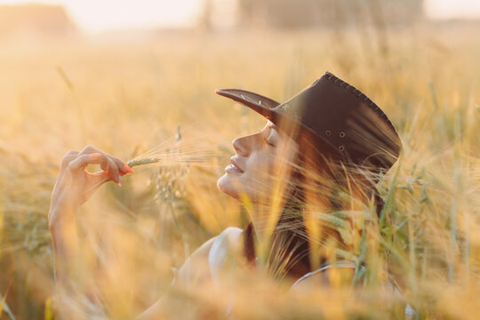 Woman farmer in cowboy hat at agricultural field on sunset.