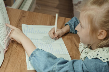 Girl writing in notebook and pointing at book. Preschooler learning to read and write. Early child education development concept.