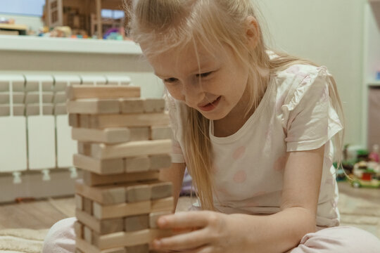 Caucasian girl intently playing a wooden block stacking game. Childhood development and entertainment concept for indoor activity.