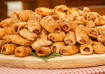 Assorted baked pastries piled on wooden board with sesame seeds and golden crusts