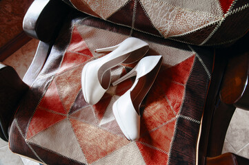 A pair of white high heels elegantly placed on a patterned leather armchair, exuding sophistication...