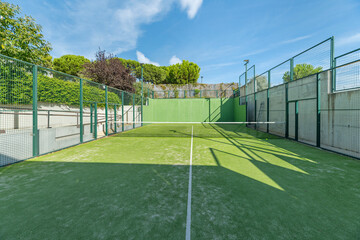 A tennis and padel court with a green artificial grass surface on a beautiful summer day