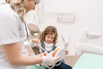 Female dentist teaching oral hygiene to little girl using tooth model in dental clinic