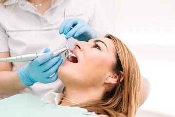 Dentist using dental drill on female patient in clinic