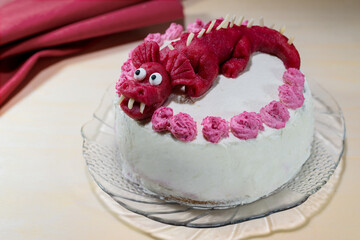 Homemade cake for a birthday party for children decorated with a red dragon made of marzipan, creative baking concept, copy space, selected focus