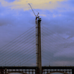 Fototapeta premium Construction Crane on Bridge Tower Against Blue and Gold Sky