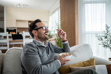 Naklejka premium Man laughing on sofa watching TV and eating snack