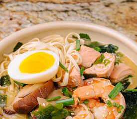 Delicious bowl of ramen with shrimp, salmon, egg, and vegetables