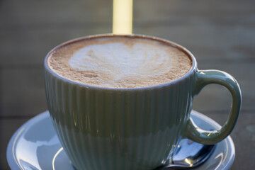 A ribbed ceramic cup filled with frothy cappuccino sits on a matching saucer, topped with heart-shaped latte art.