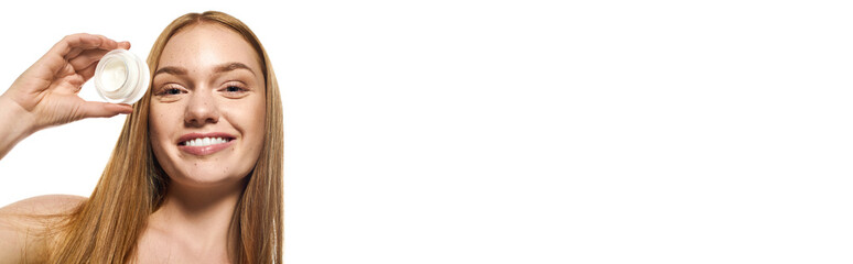 Young woman with radiant smile showcasing a skincare product in a bright setting