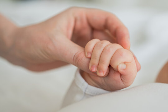 Happy family. Tiny newborn infant baby little hand on mother hand palm. Newborn baby holding parent finger after birth. Mom baby at home. Support protection of new life. Handle with care