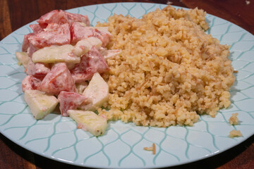 A plate of creamy tomato-cucumber salad and cooked bulgur sits on a patterned light blue dish.