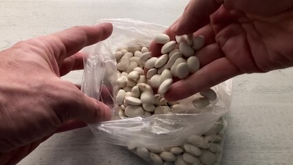 Inspecting Raw Ingredients: A close-up of a person's hand sorting through a plastic bag of dry white beans, carefully checking the quality of the legumes before cooking a healthy meal