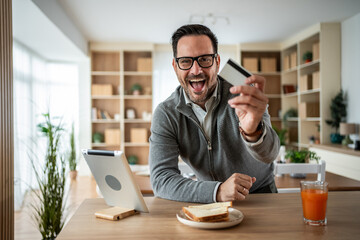 Smiling man showing credit card for online shopping at home