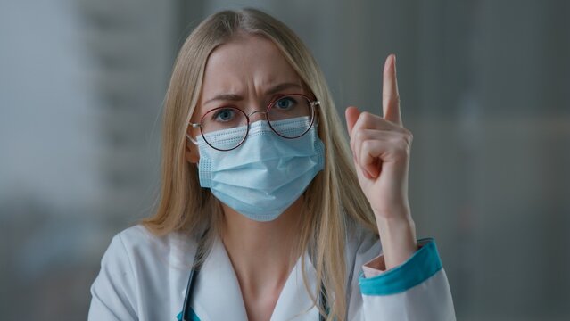 Caucasian doctor woman in medical face mask shaking finger talking looking at camera negative scolding female nurse girl scientist medicine in clinic hospital talk about health video call conference