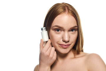 Fototapeta premium Young woman holding a beauty product with a confident smile in a bright setting
