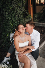 Naklejka premium Wedding photography, portrait of happy smiling newlyweds, fashionable groom and beautiful cute brunette bride, hugging outdoors on the street in the city, in the park.