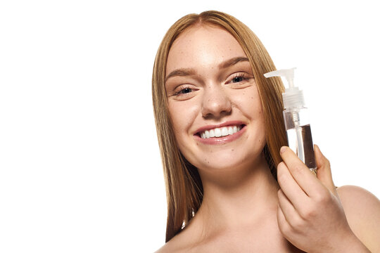 Young woman showcasing glowing skin and a clear smile while holding a skincare product
