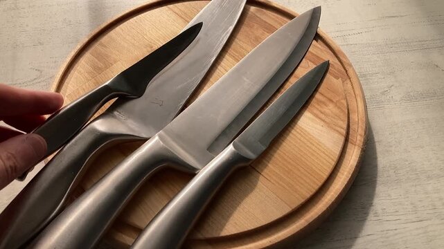 Chef's Essentials: A person's hand carefully arranging a set of professional stainless steel kitchen knives and a carving fork on a round wooden cutting board in preparation for cooking