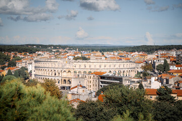 Obraz premium Panoramic cityscape of Pula, Croatia, featuring the ancient Roman amphitheater surrounded by traditional buildings with orange rooftops on a bright summer day.
