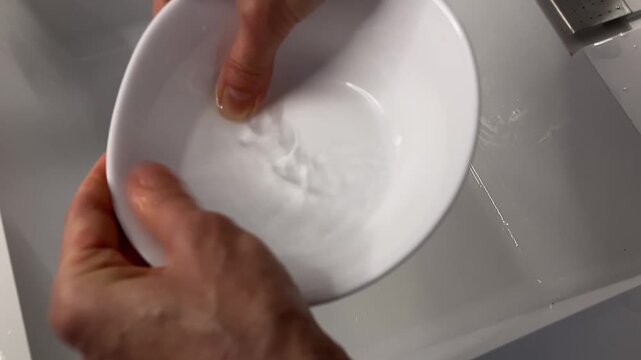 Washing a Ceramic Bowl: A close-up of a person's hands diligently scrubbing and rinsing a white ceramic bowl with water, with the natural sound of fingers squeaking on the wet surface