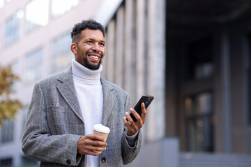 Smiling man in suit with smartphone and takeaway cup on city street, low angle view. Space for text