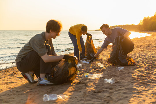Earth day. Volunteers activists team collects garbage cleaning of beach coastal zone. Woman mans puts plastic trash in garbage bag on ocean shore. Environmental conservation coastal zone cleaning