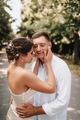 Fototapeta premium Wedding photography, portrait of happy smiling newlyweds, fashionable groom and beautiful cute brunette bride, hugging outdoors on the street in the city, in the park.