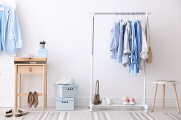 Different stylish clothes hanging on rack, bags and shoes near white wall indoors