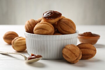Delicious nut shaped cookies with boiled condensed milk and spoon on white wooden table, closeup