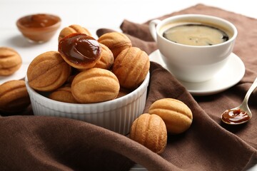 Delicious nut shaped cookies with boiled condensed milk served with coffee on white table, closeup