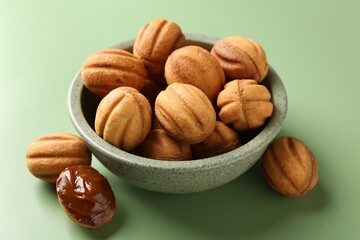 Delicious nut shaped cookies with boiled condensed milk in bowl on green background, closeup