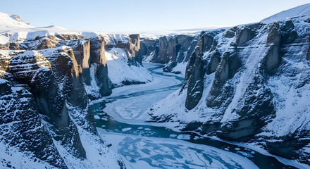 A majestic snow-covered canyon with a winding, partially frozen river illuminated by the low winter sun.