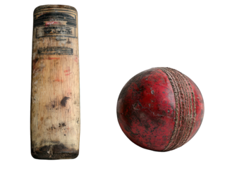 Worn cricket bat stands next to a weathered red leather cricket ball