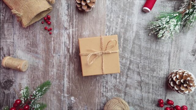 Slow motion top view shot as the camera pulls away from a wrapped gift on a rustic wooden table, showing festive flat lay holiday details