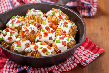 Crispy golden potatoes topped with sour cream, bacon bits, and green onions in a cast iron skillet