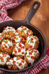 Crispy golden potatoes topped with sour cream, bacon bits, and green onions in a cast iron skillet