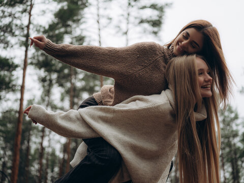 Happy lesbian couple piggyback ride laughing arms outstretched forest - Powered by Adobe