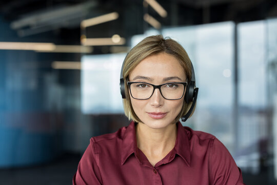 Woman with headset and glasses looks calmly at camera in corporate office, conveying professional, helpful customer service and confident support for call center or remote consulting roles