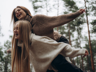 Happy lesbian couple piggyback ride laughing arms outstretched forest