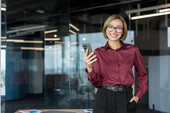 Confident businesswoman smiling and holding a smartphone, representing success, communication, and connectivity in a contemporary workplace while managing business