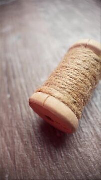 Vertical slow motion macro shot of twine spool on wooden surface with soft light as camera moves left