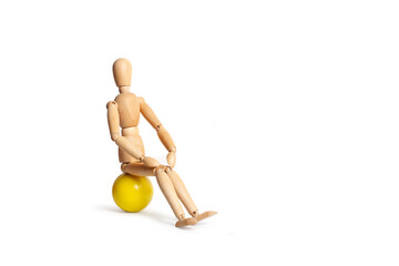 A wooden mannequin sitting on a yellow ball isolated on a white background with copy space