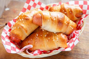 Savory hot dogs wrapped in golden, flaky dough served in a checkered basket at a casual dining spot