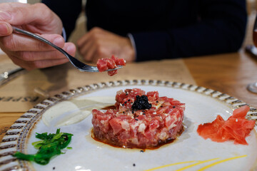 Person enjoying fresh red tuna almadraba tartare with caviar and seaweed on a plate