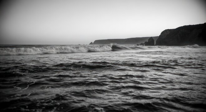 Black and white seascape; waves rolling toward the shore, cliffs in distant view