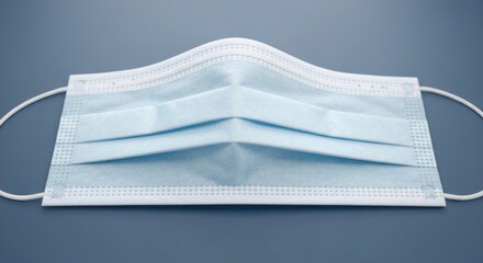 Light blue surgical mask with elastic ear loops on a gray surface, close-up