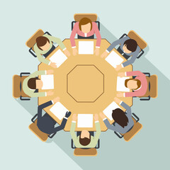 Overhead view of a diverse business team seated around a large octagonal table, engaged in a professional meeting, discussion, or collaboration at the office