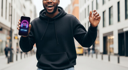 Cheerful man showing a mobile music gift card app in a city street for digital gifting.